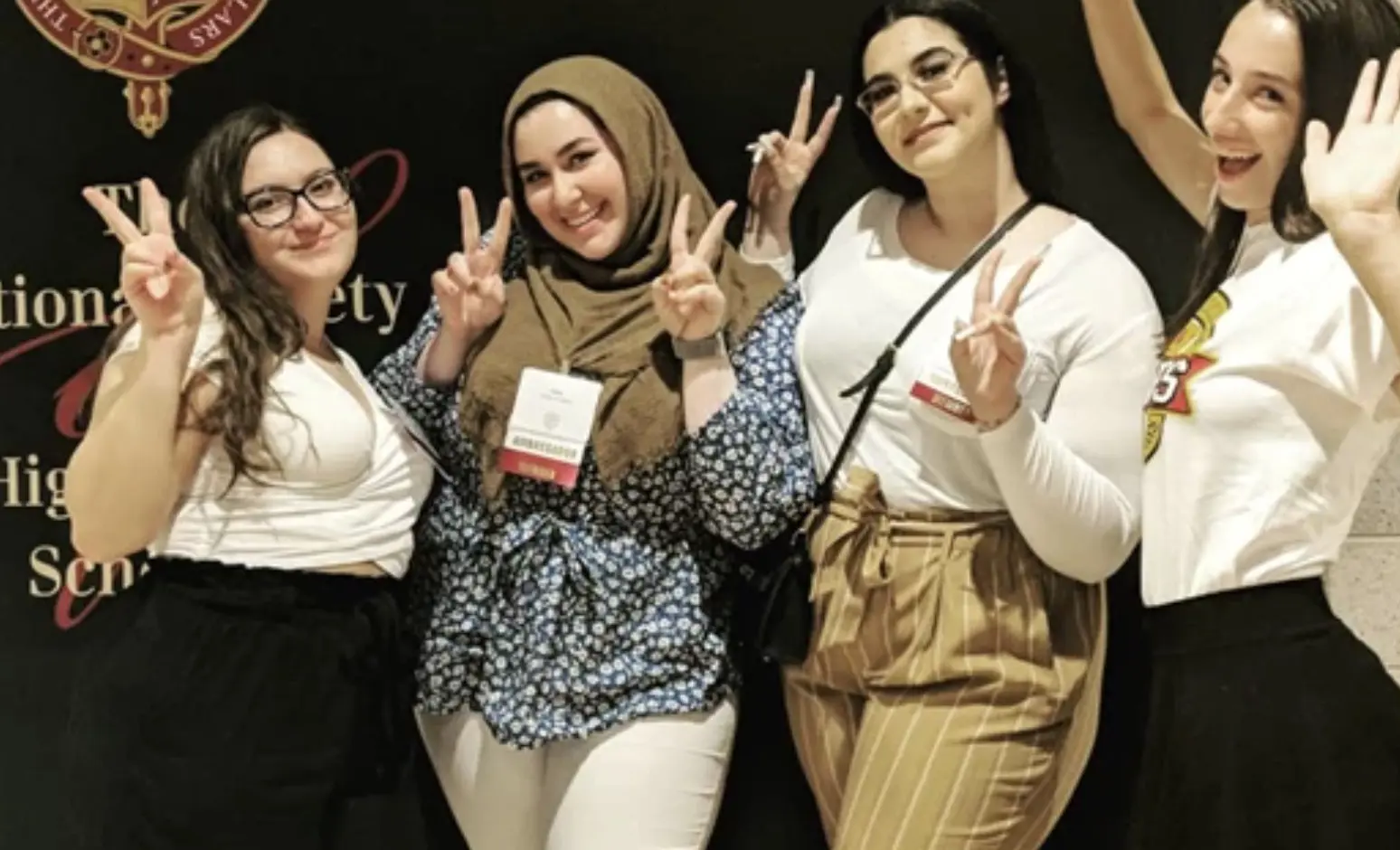 Student wearing head scarf with friends holding up peace sign